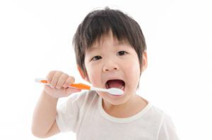 Young toddler opening his mouth and sticking in a large, orange toothbrush while slightly smiling a silly grin