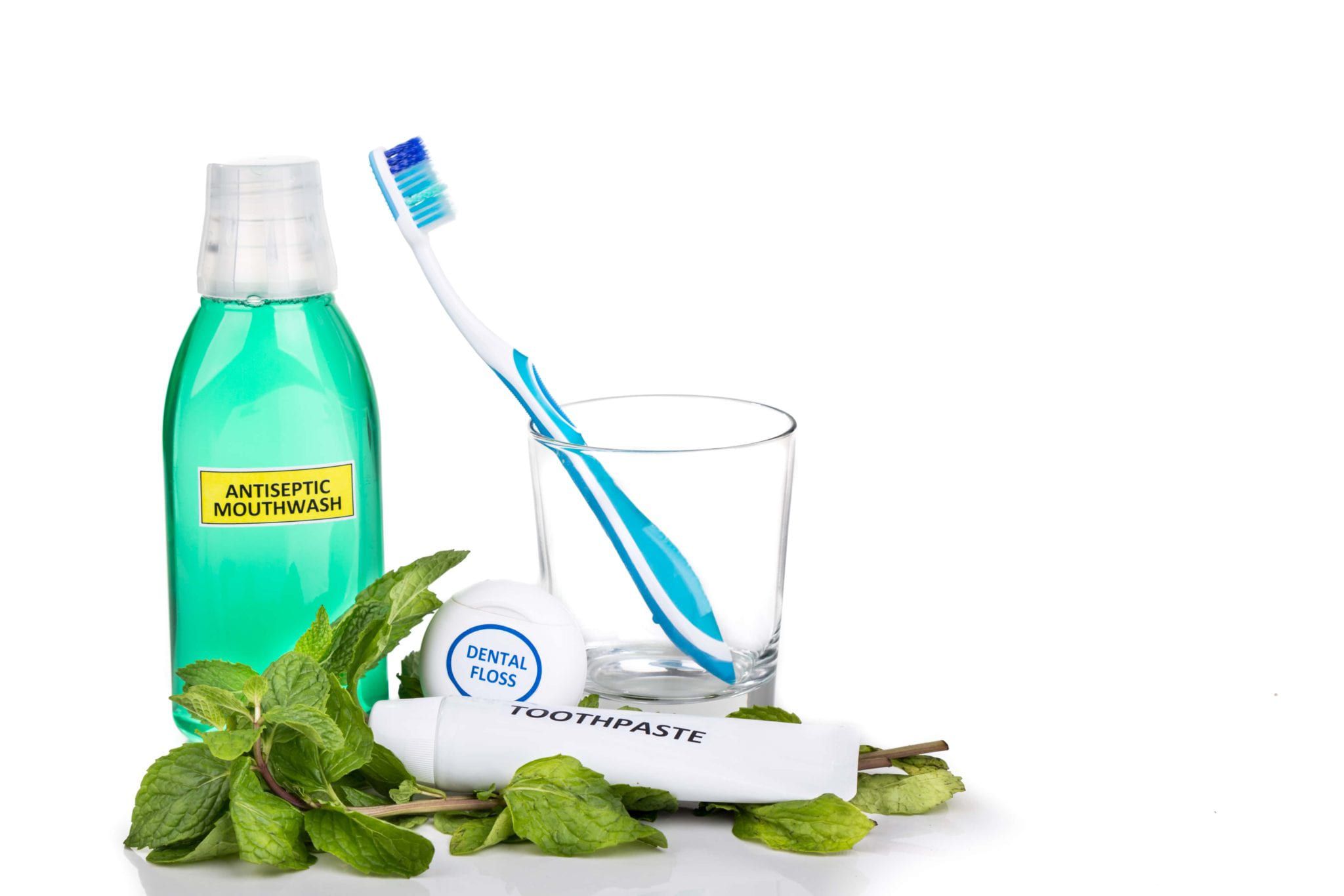 Mouthwash, toothbrush, floss, and toothpaste on a white background surrounded by mint leaves